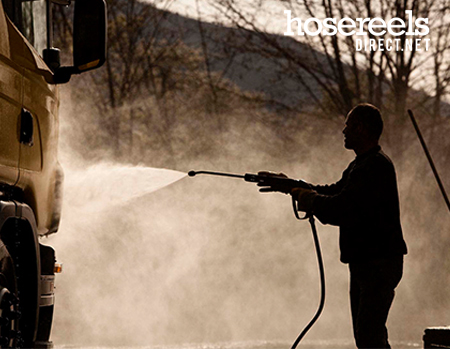 Silhouette of a man using a jet wash reel and lance to powerwash a lorry