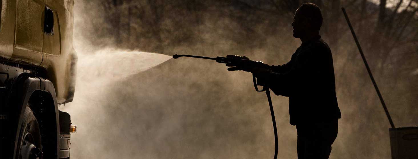 A man using a jet wash lance to clean a lorry